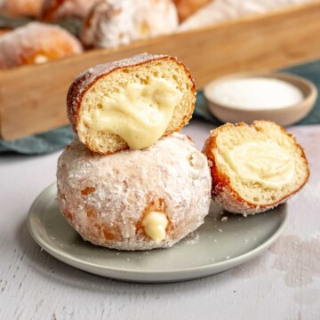 Custard donuts stacked on a plate. The top one is cut open to show the pastry cream coming out.