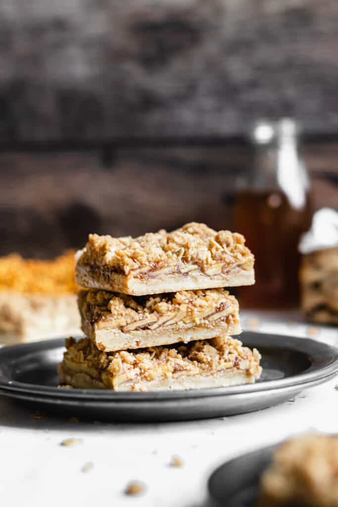 a stack of apple crisp bars on a place with apple cider in the background 