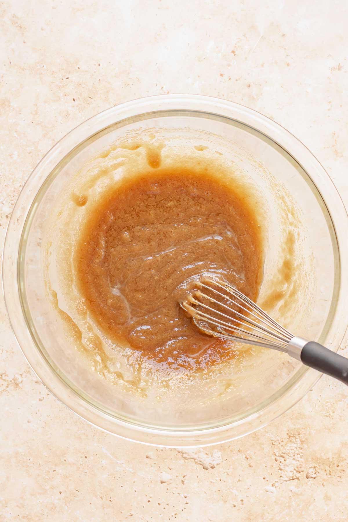 A whisk mixes brown sugar and butter in a bowl.