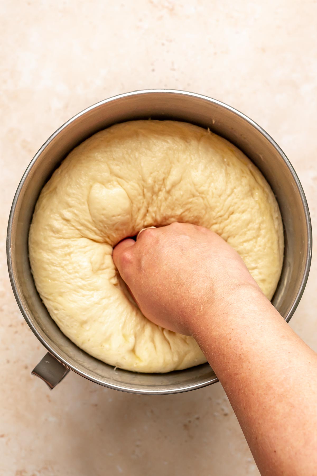 A hand punches down risen donut dough in a bowl.