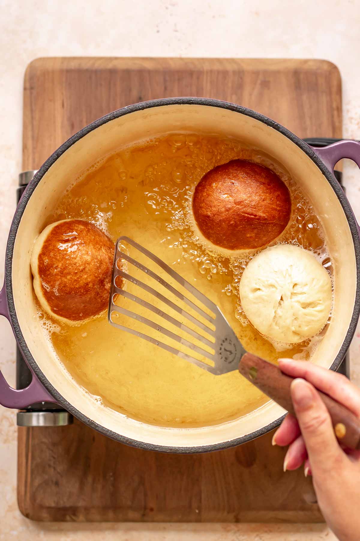 A spatula flips frying donuts in a dutch oven.