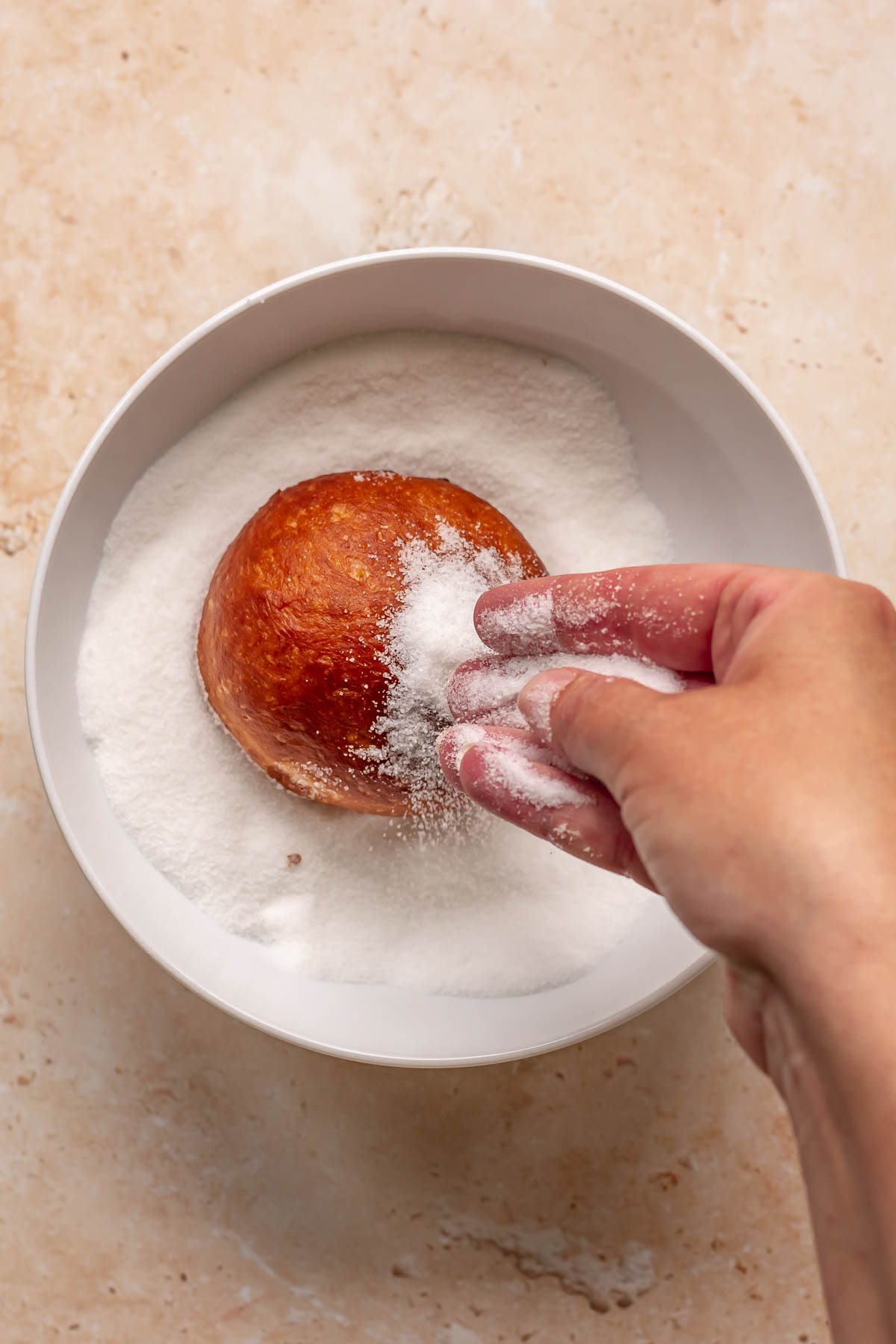 Donut in a bowl getting covered with sugar.
