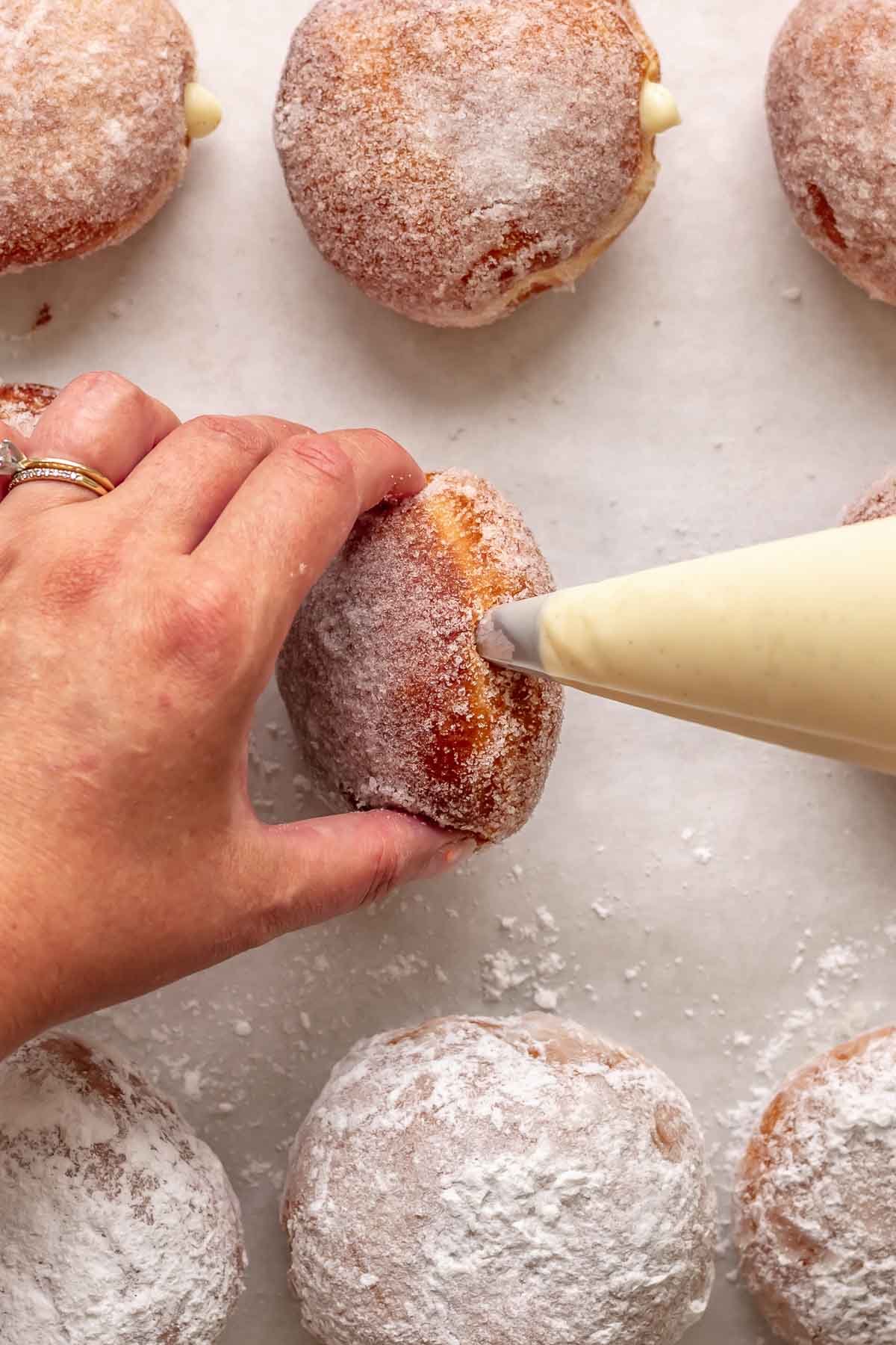 A hand pipes pastry cream into a fried brioche donut.