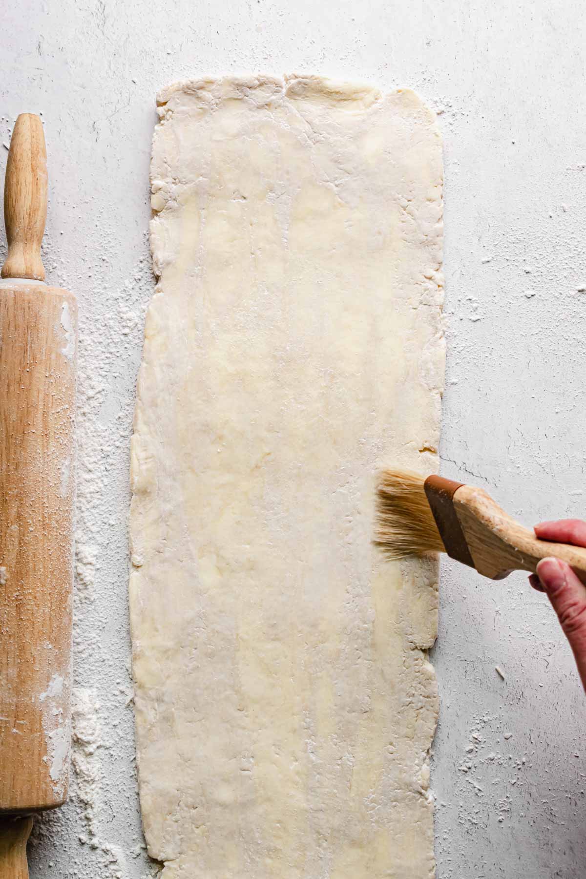A pastry brush removes flour from the rolled out rough puff pastry.
