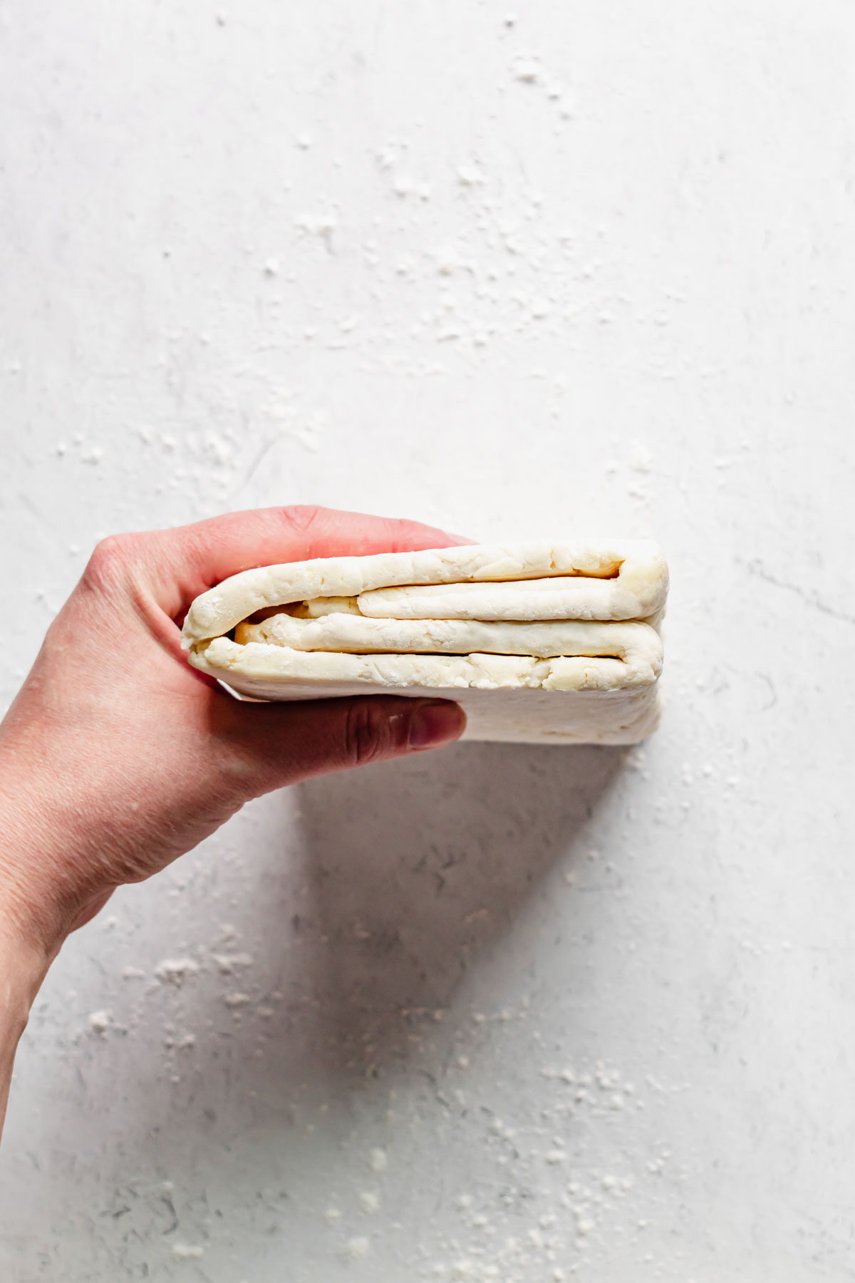 A hand holds the dough up to show the trifold inside.