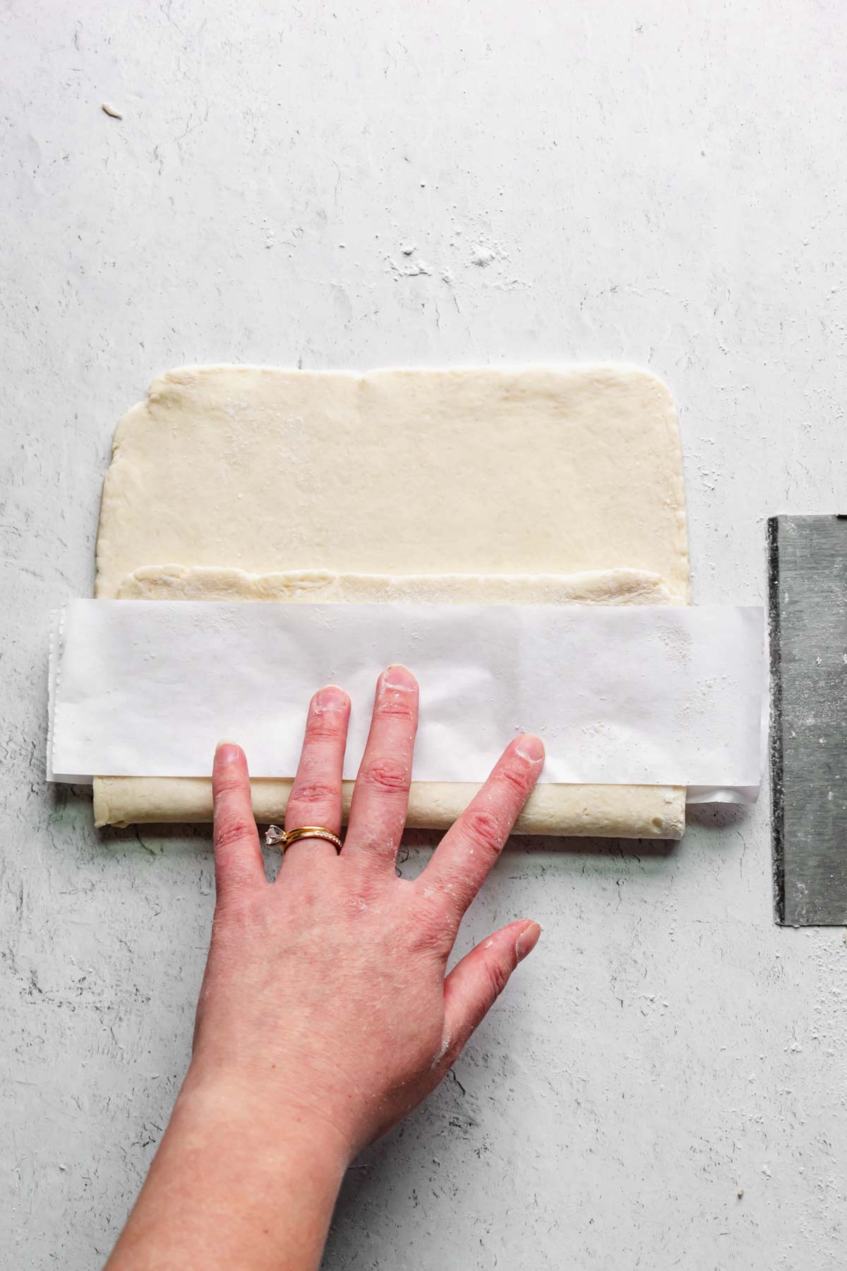 One third of pastry is folded over the parchment, then another strip of parchment is added on top.
