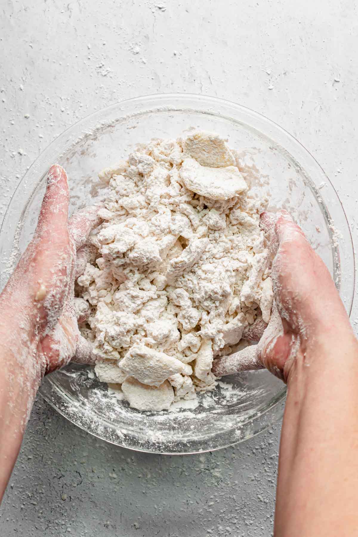 Two hands toss the butter, flour and water together.