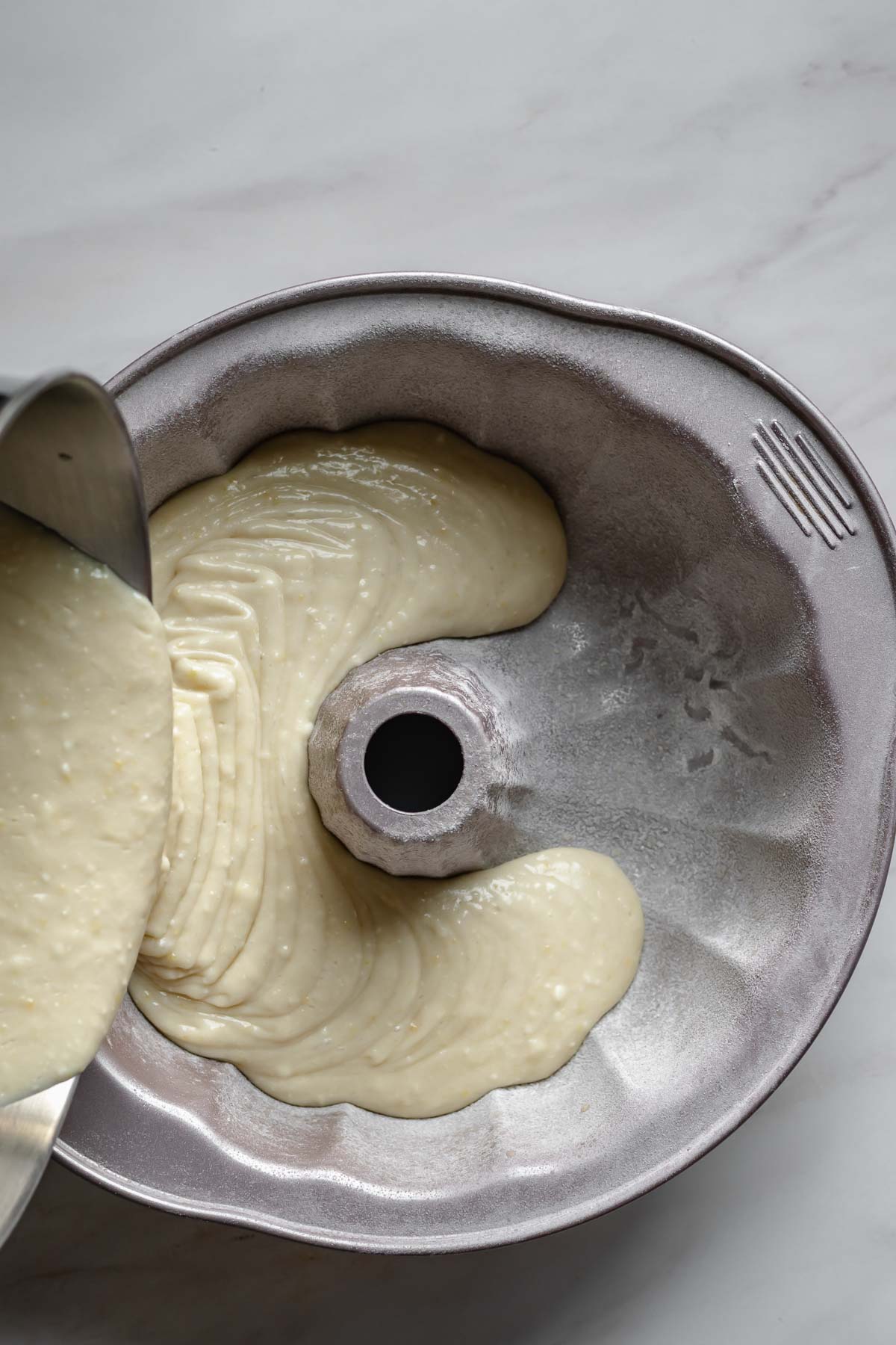 Lemon ricotta cake batter pouring into a prepared bundt pan.