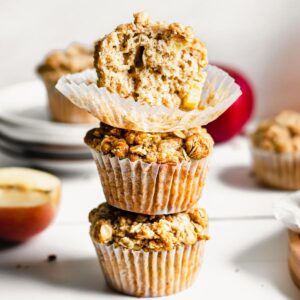 Stack of three apple crumble muffins. The top has a bite removed.