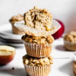 Stack of three apple crumble muffins. The top muffin has a bite removed