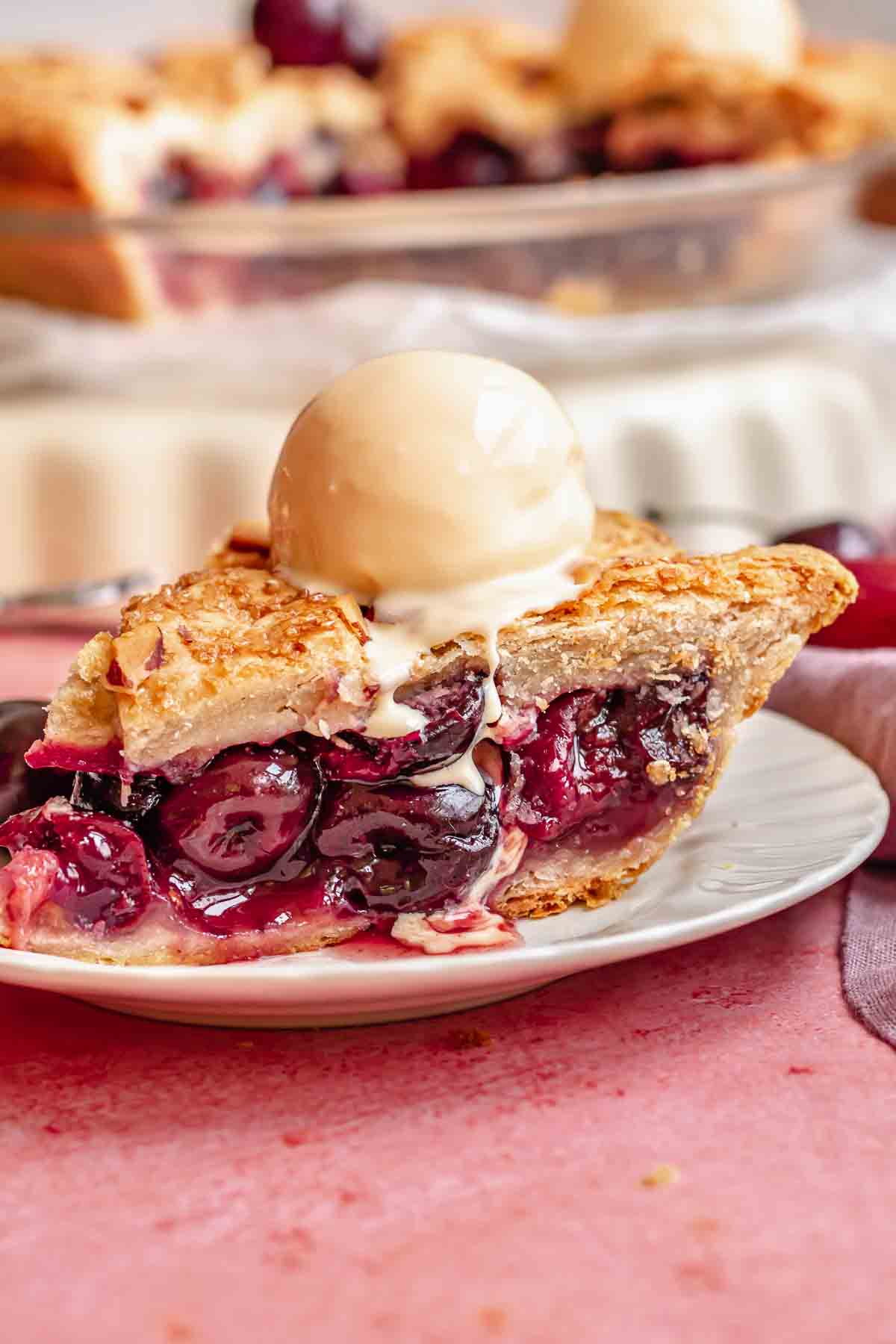 A slice of cherry rhubarb pie on a plate with a scoop of ice cream on top.