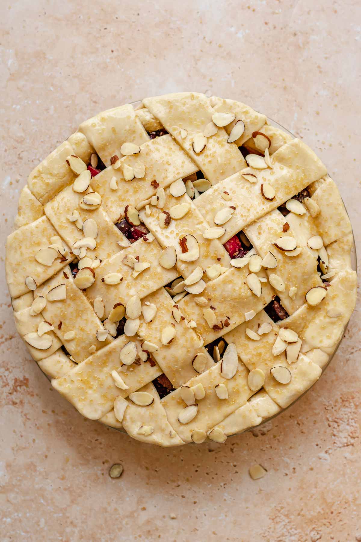 Pre-baked cherry rhubarb pie with coarse sugar and sliced almonds on top.