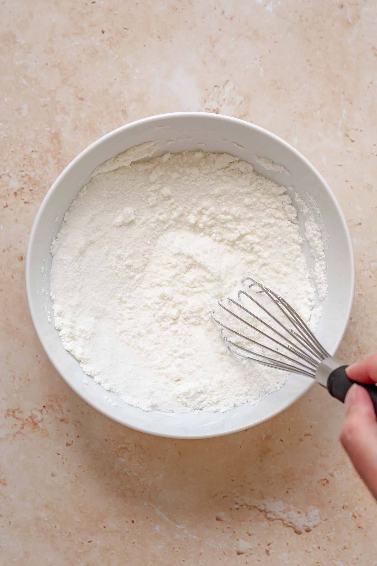 A hand whisks together sugar and cornstarch in a bowl.