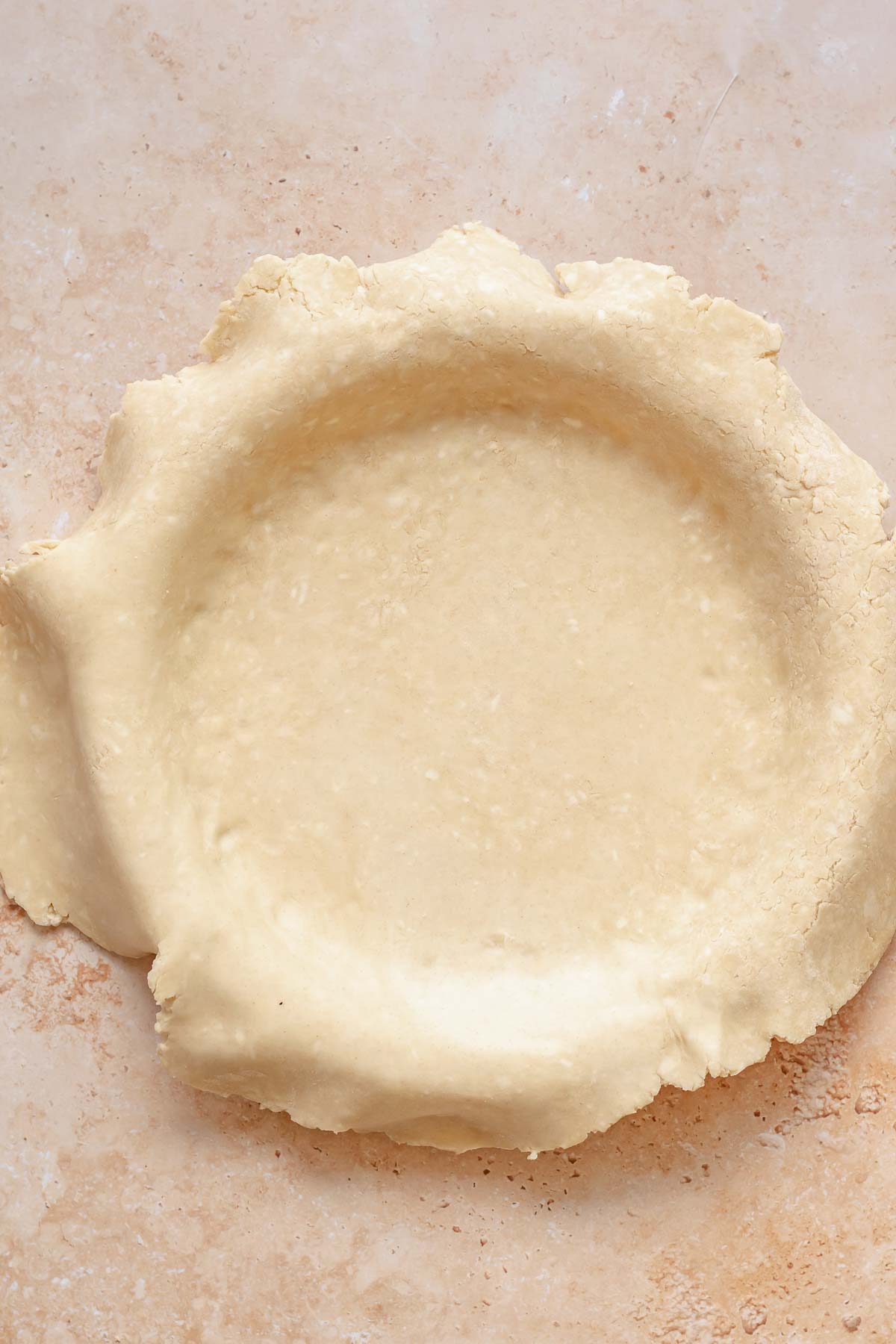 Pie crust fitted into a pie dish with pastry hanging over the sides.