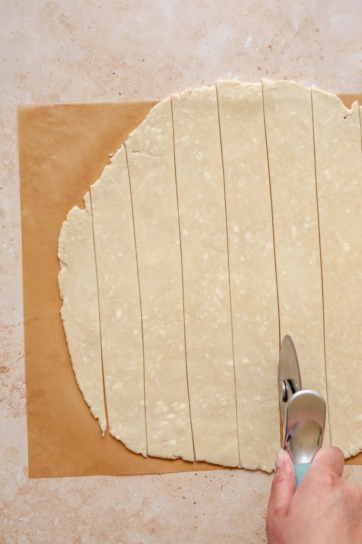 A pizza roller cuts rolled out pie crust into lattice strips.