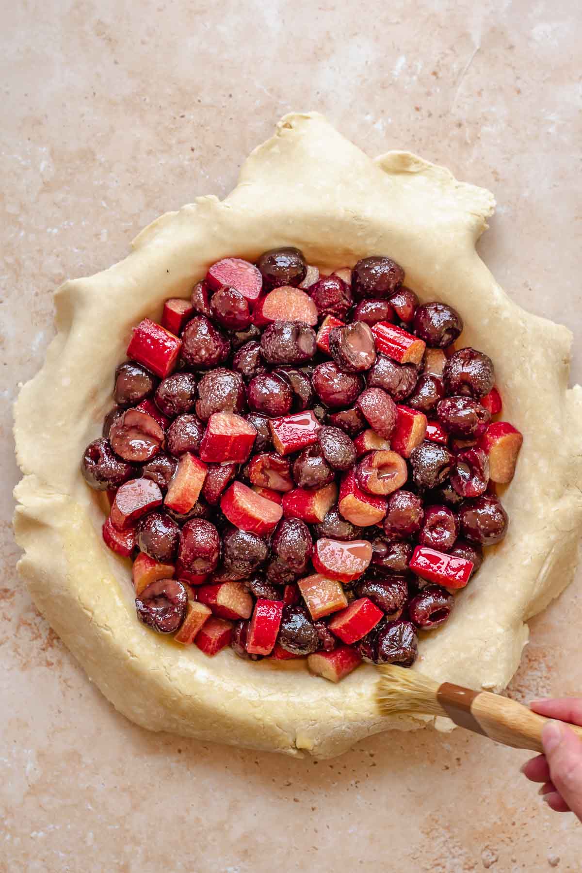 Cherries and rhubarb in the center of the pie crust. A pastry brush adds egg wash to the edges.