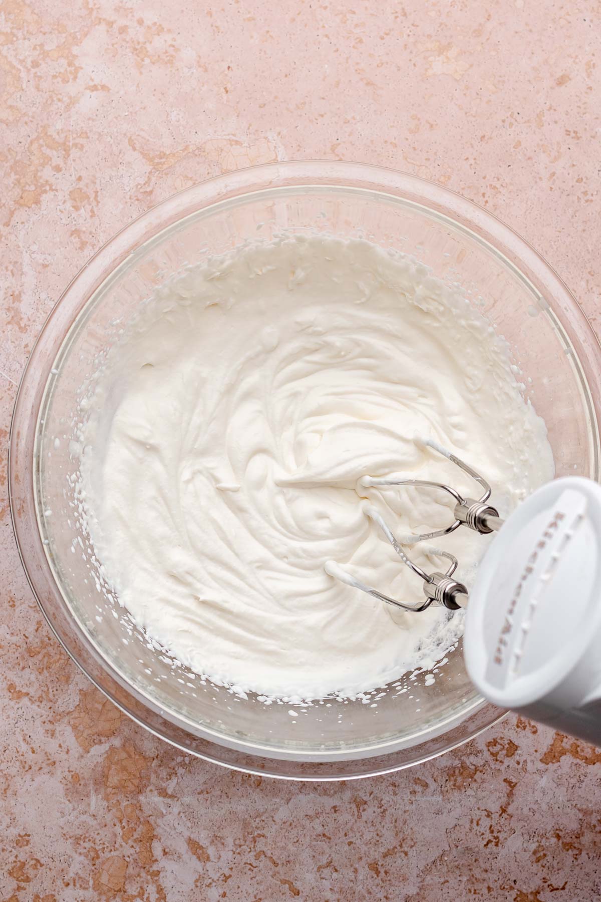 A hand mixer beats whipped cream in a bowl.