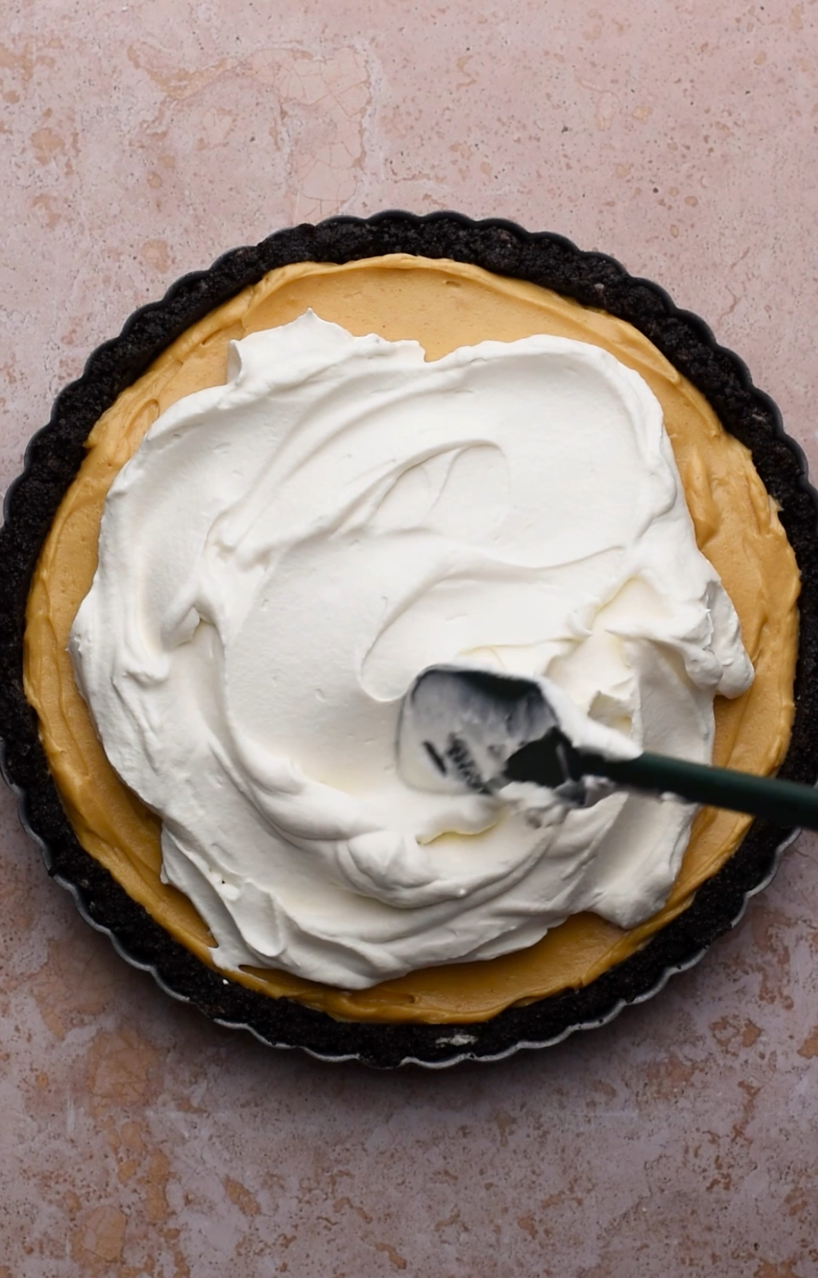 A spatula spreads whipped cream onto a chocolate peanut butter tart.