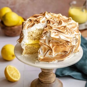 Lemon meringue cake on a stand with a slice removed.