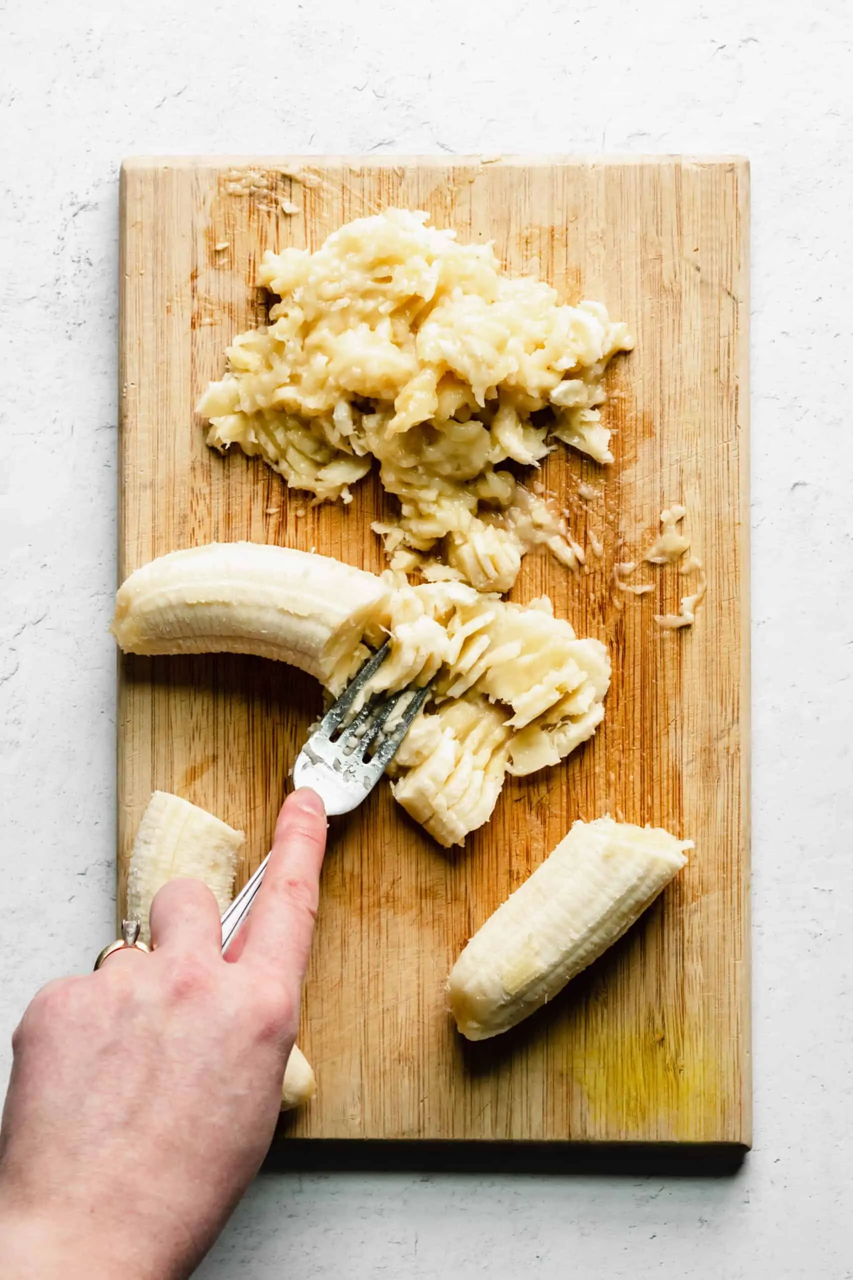 A hand mashed bananas on a cutting board with a fork.