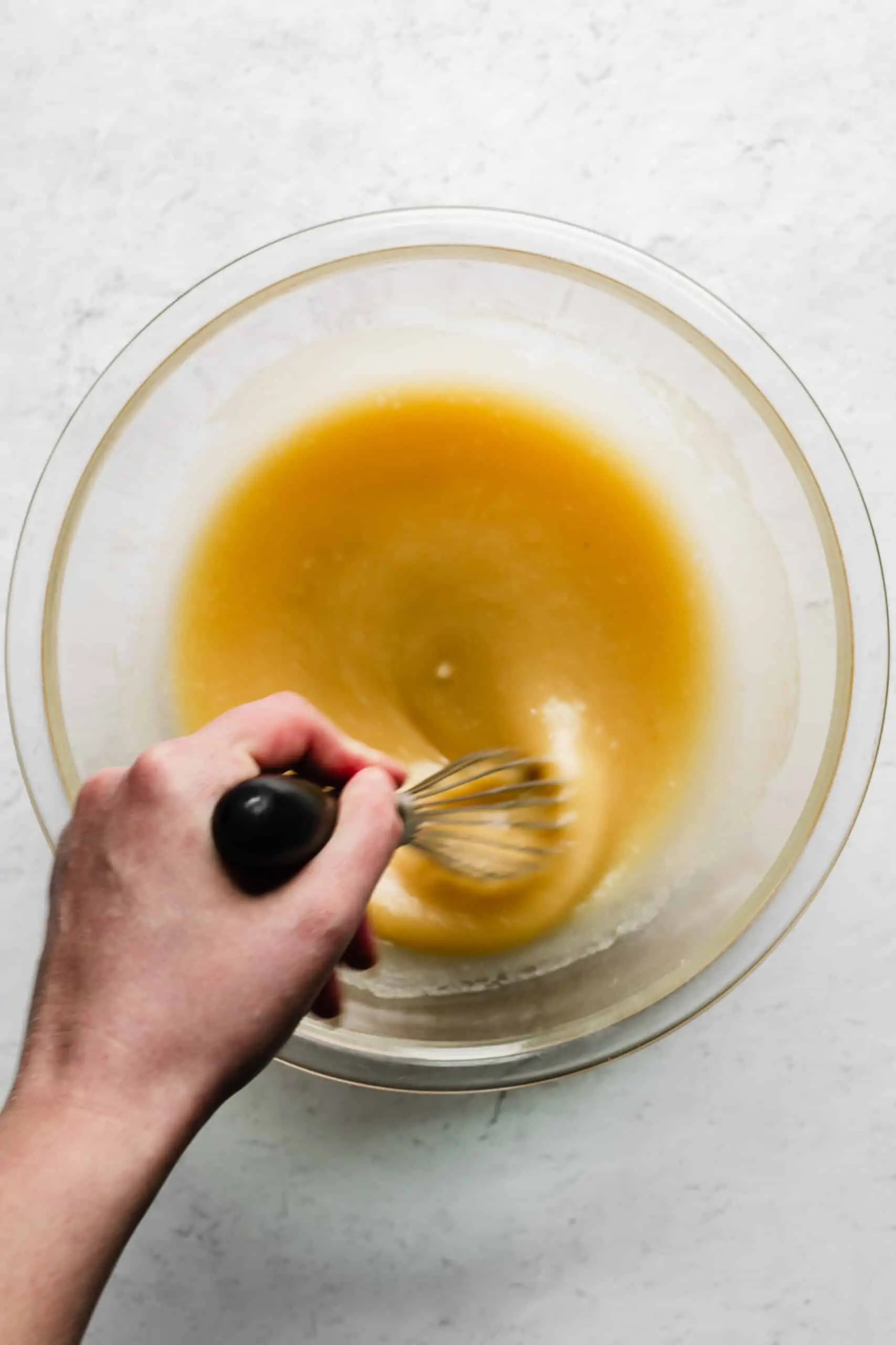A hand whisks together wet ingredients for muffin batter.