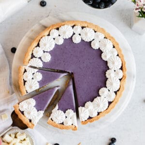 Blueberry white chocolate ganache tart with three pieces sliced. One is being removed.