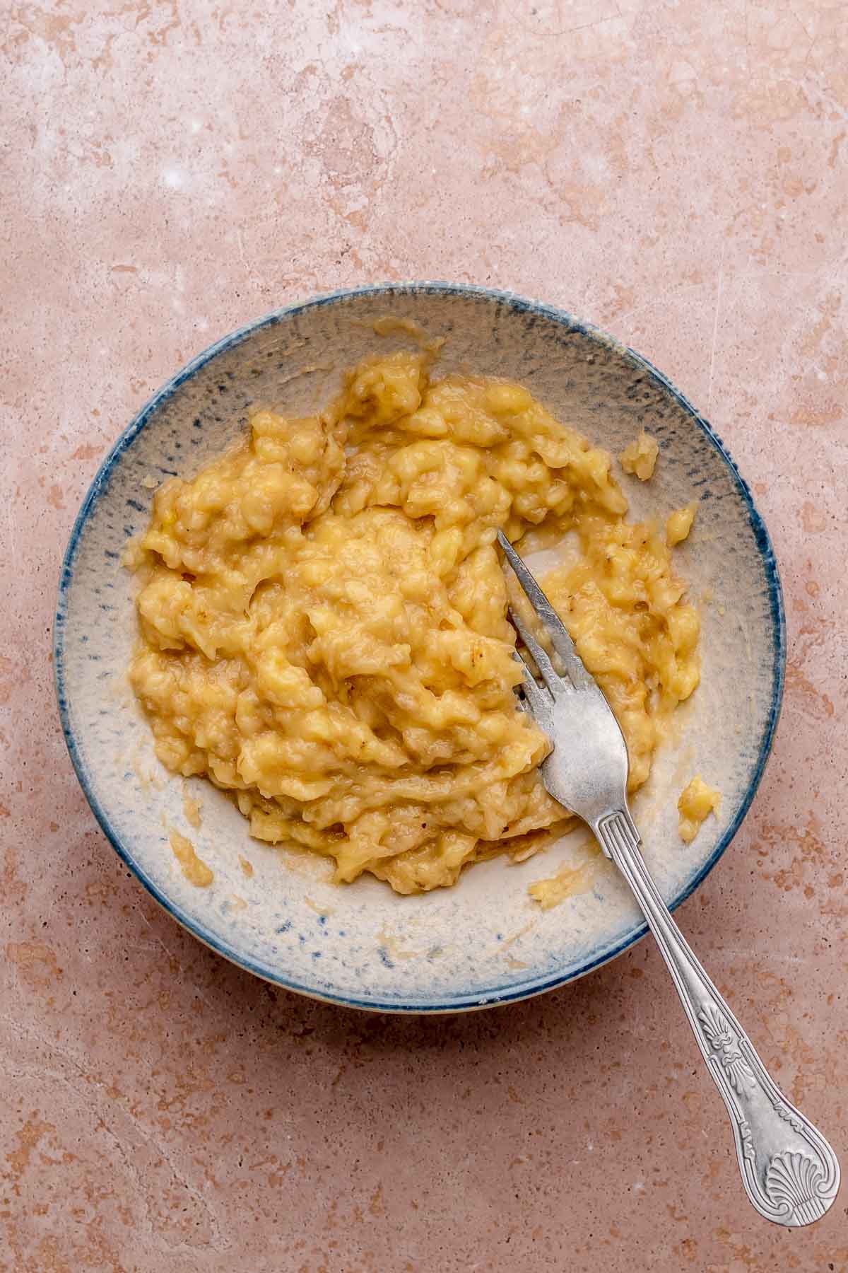 A fork mashes bananas in a bowl.