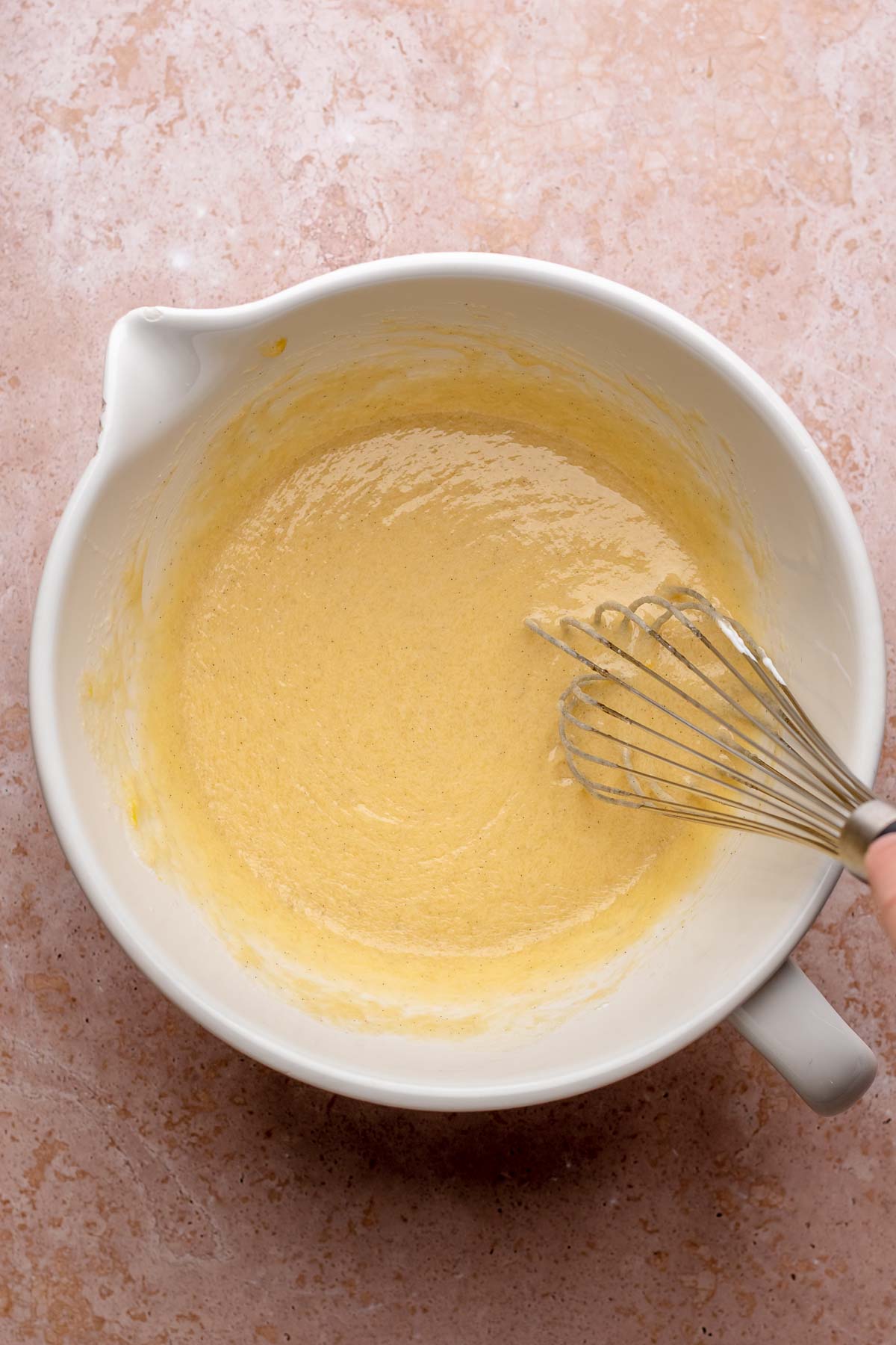A whisk mixes banana muffin batter in a bowl.