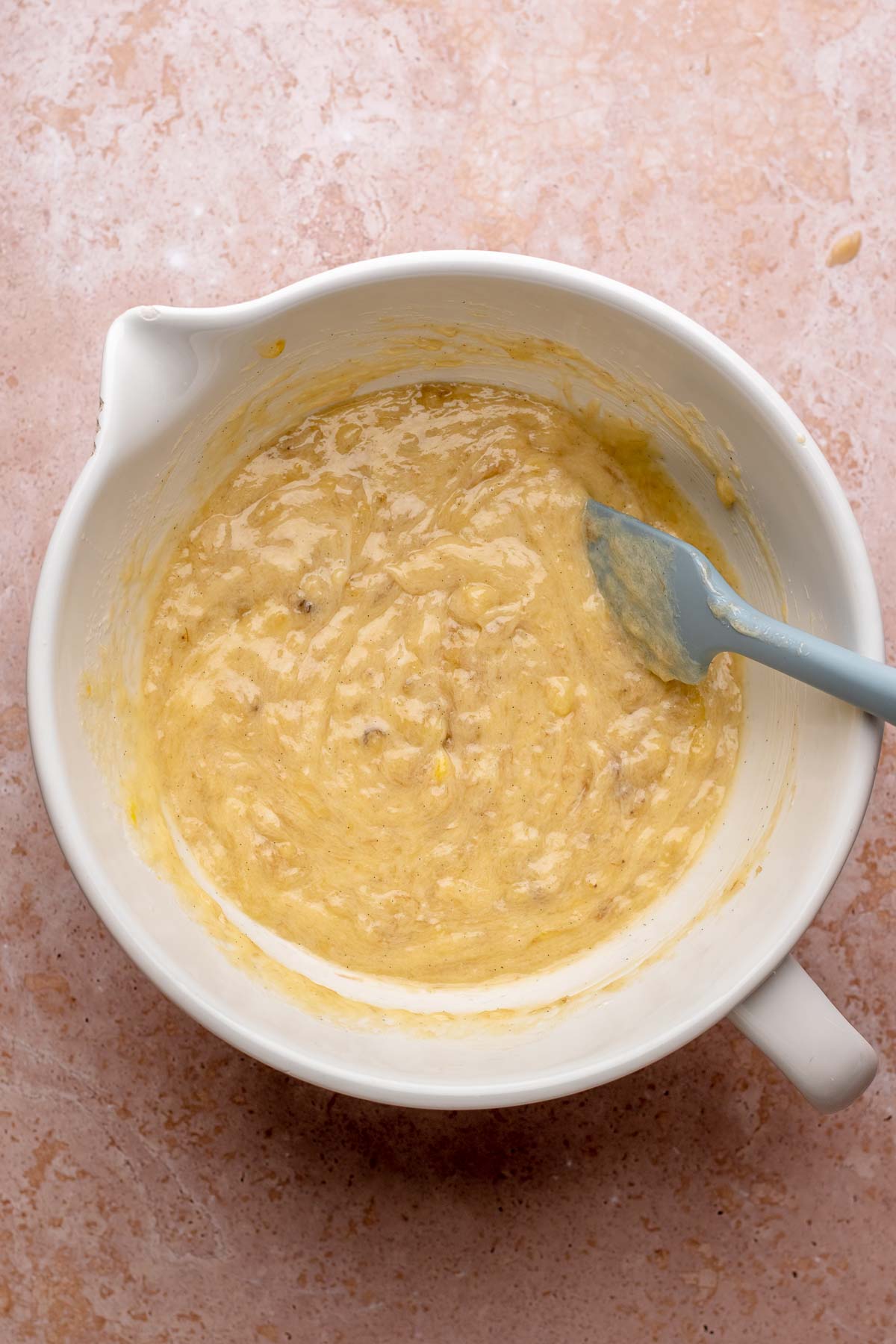 A spatula mixes wet muffin batter in a bowl.