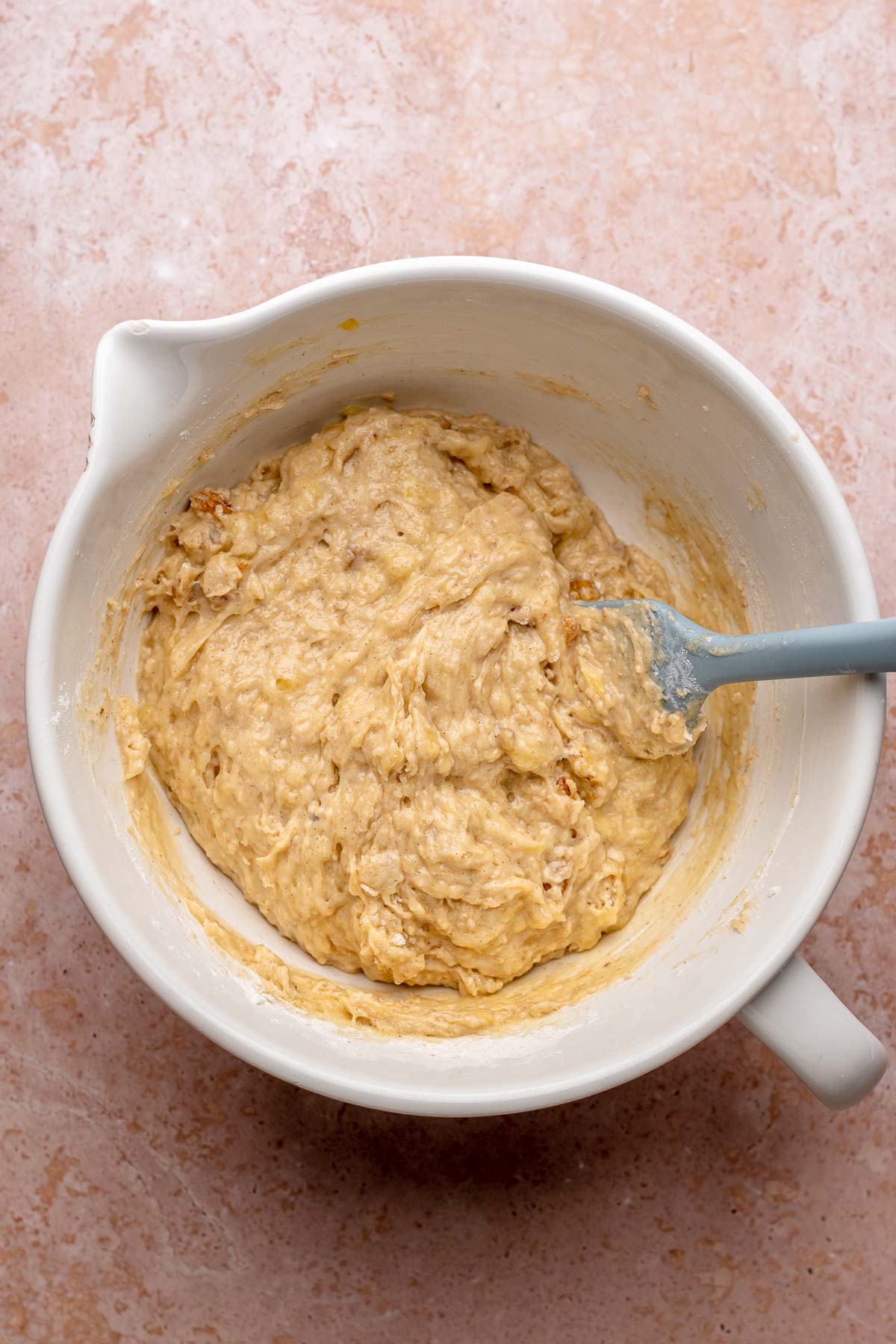 A spatula mixes banana nut muffin batter in a bowl.