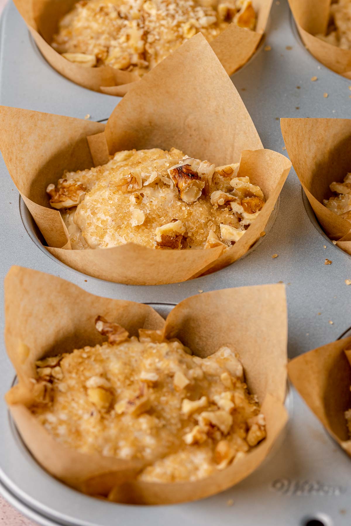 Banana muffin batter in a muffin tin before baking. Walnuts are sprinkled on top.