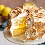 Lemon meringue cake on a stand with a slice removed.