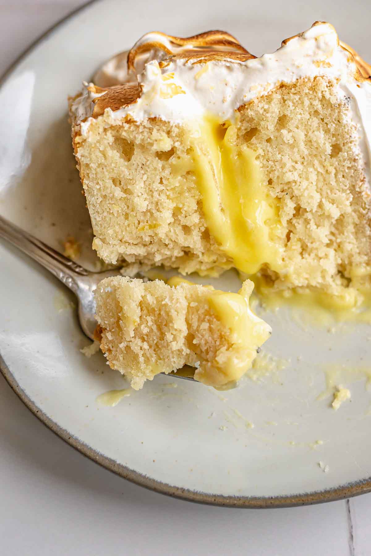 A fork has a piece of lemon meringue cake on a plate.