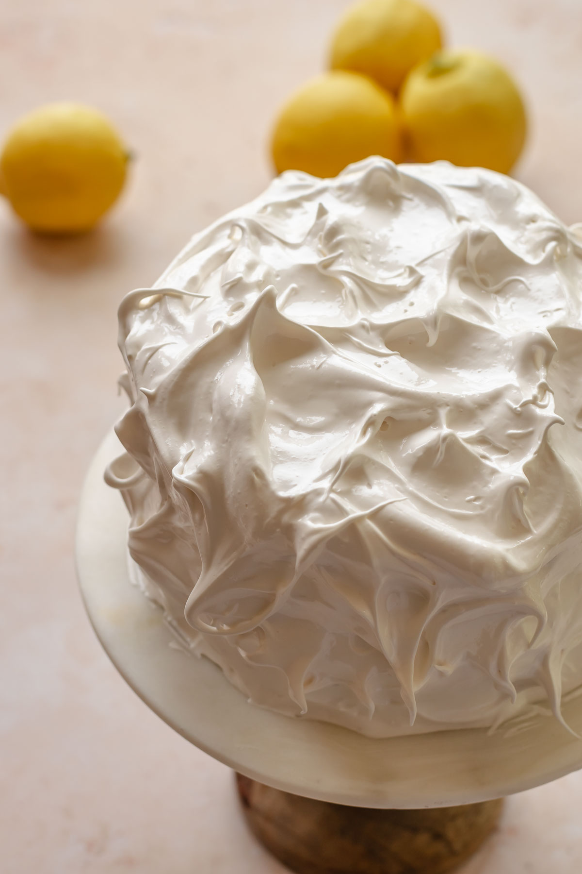 Swiss meringue covered cake with peaks on a cake stand.