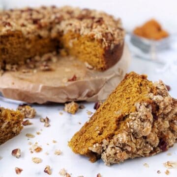A round pumpkin coffee cake with two slices taken out, laying in front of the main cake.