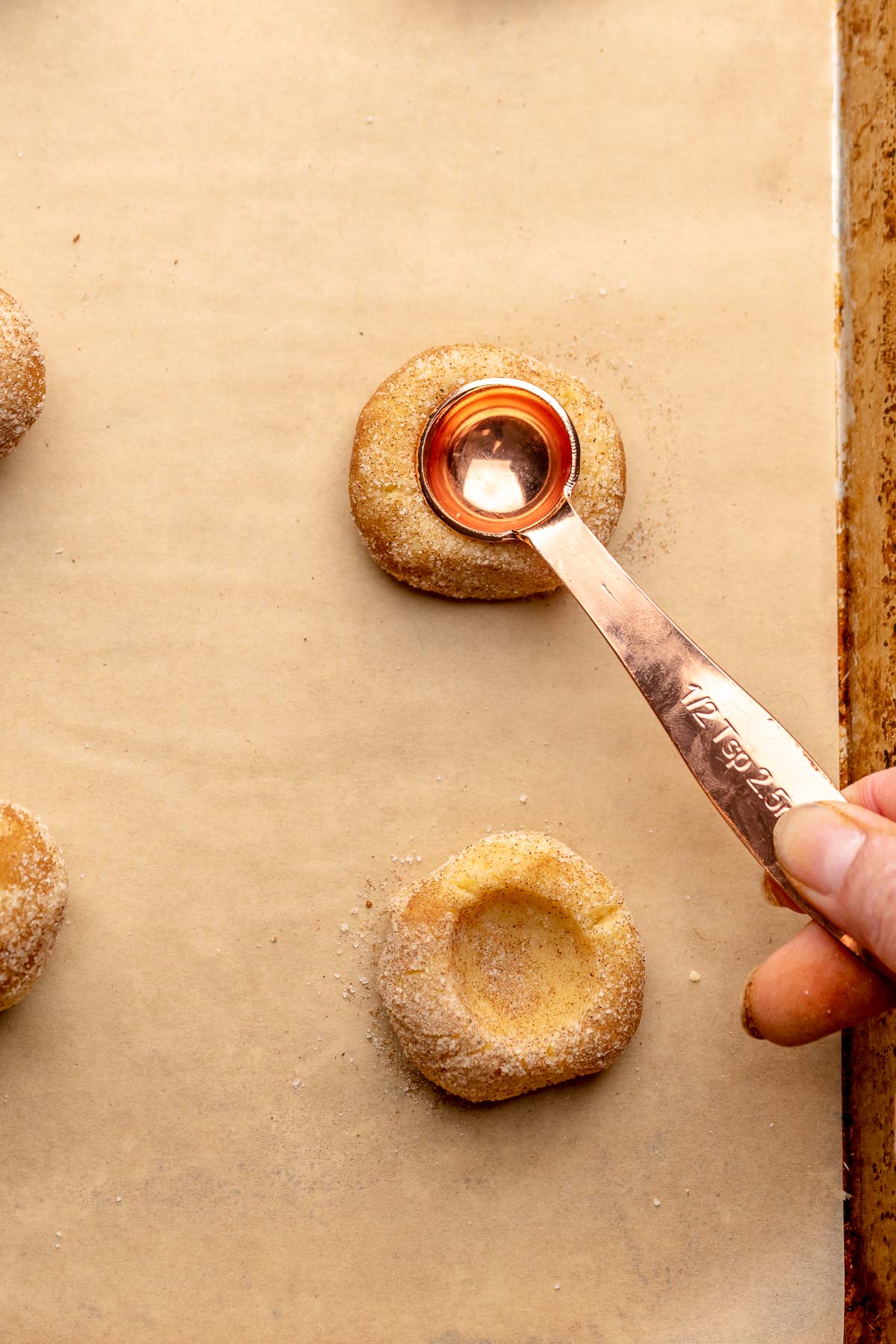 A hand uses a ½ teaspoon measure to press an opening into a dough ball.