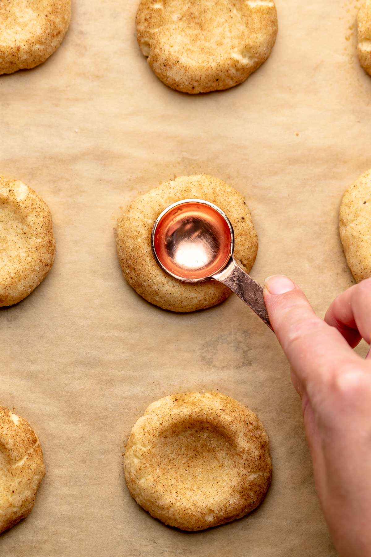 A hand uses a 1 teaspoon measure to press an opening into a baked cookie.
