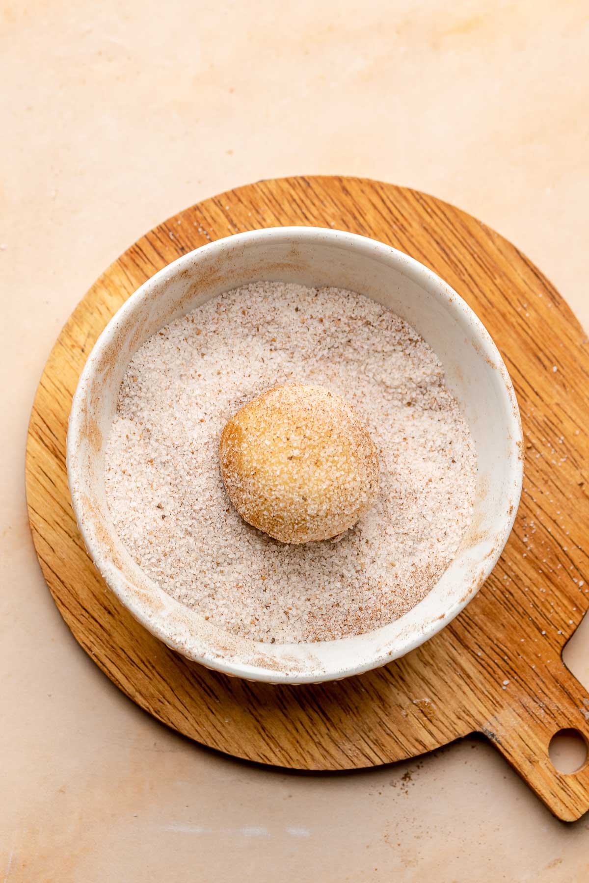 A cookie dough ball in a bowl of cinnamon sugar.