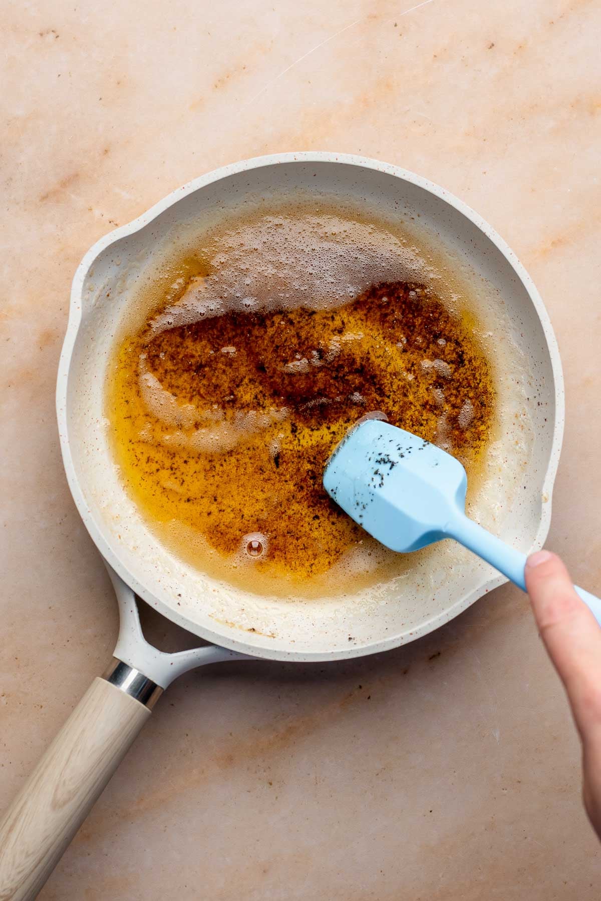 A spatula stirs brown butter in a frying pan.