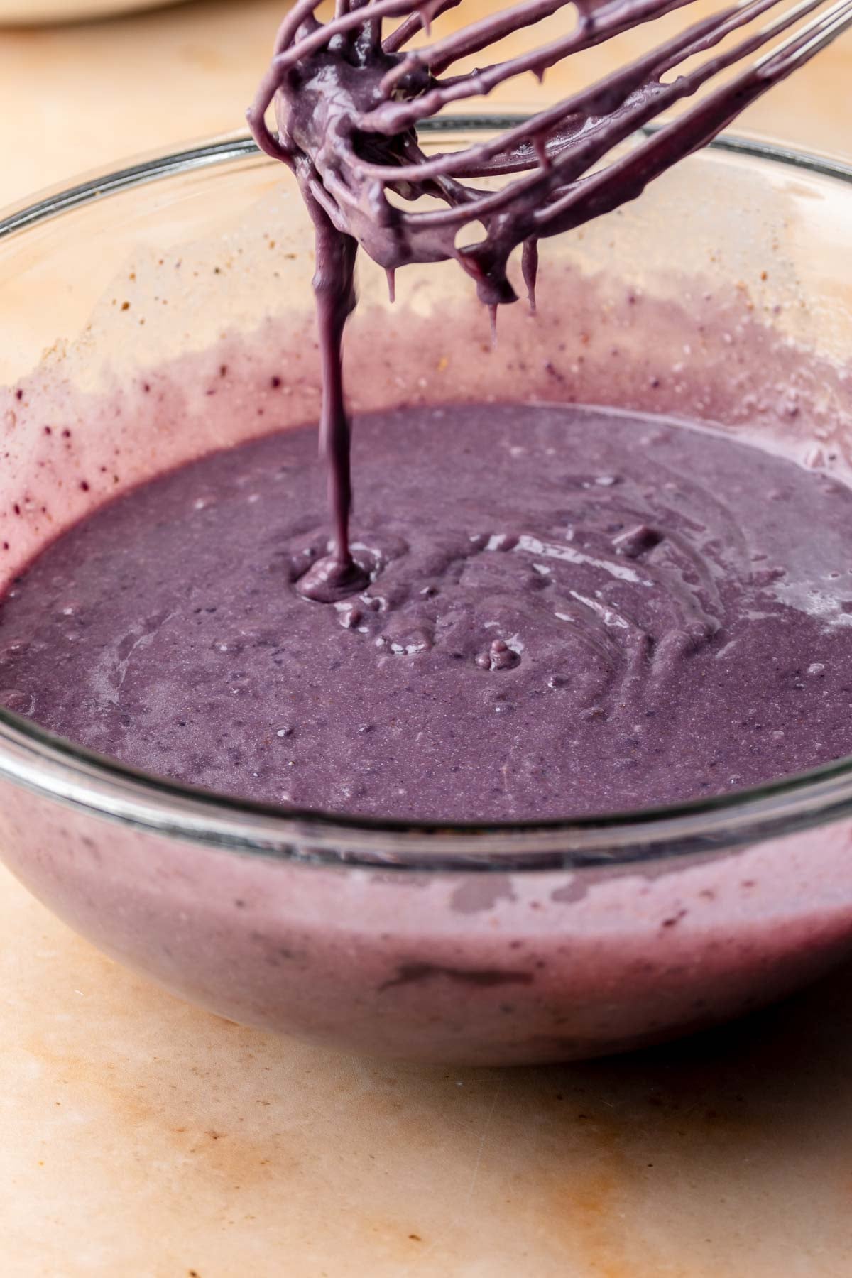 A whisk mixes purple sweet potato pie filling in a mixing bowl.