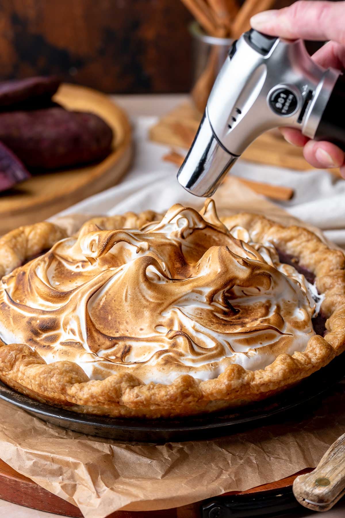 A hand torch browns meringue on top of the sweet potato pie.