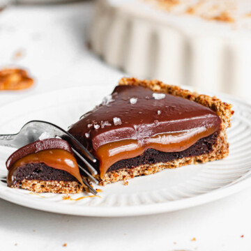 A fork cuts into a piece of caramel tart on a plate.