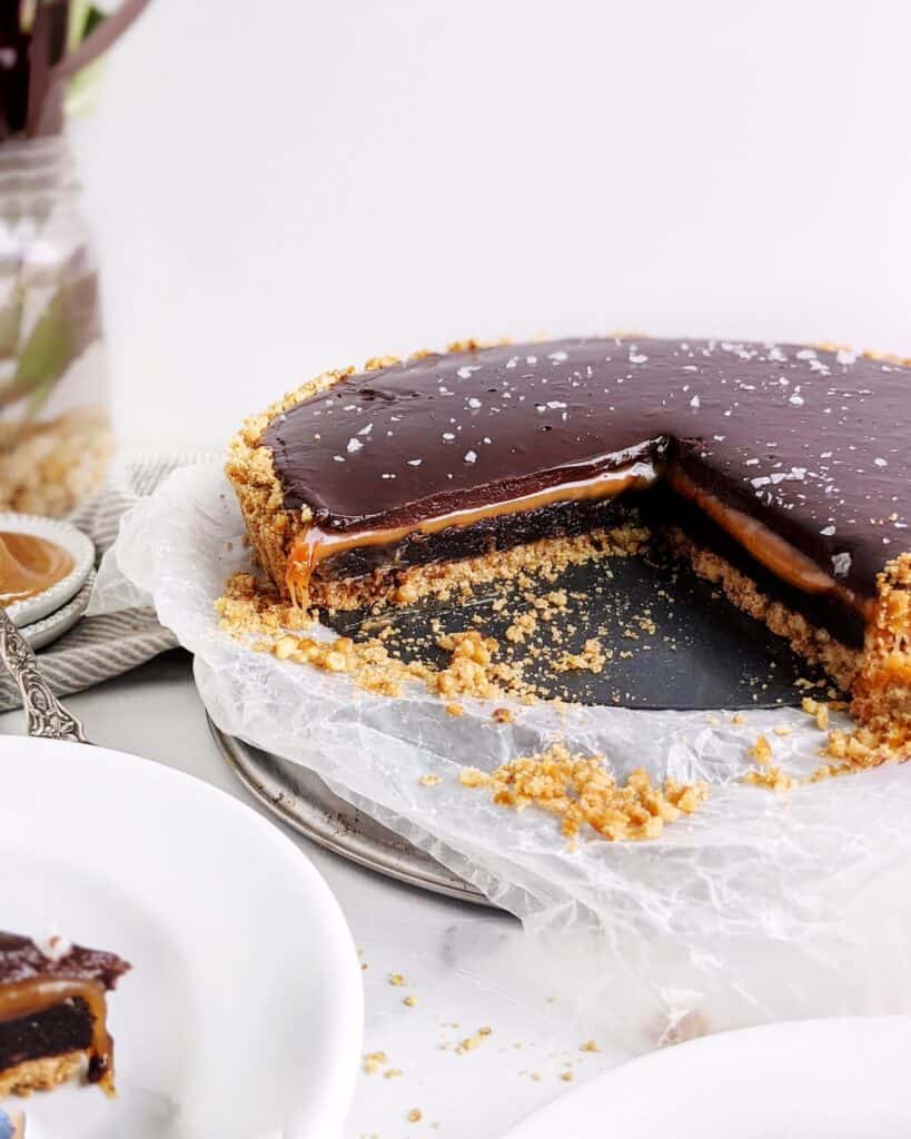 cross section of the caramel brownie pretzel pie with two slices removed. flaky salt is scattered on top of the ganache