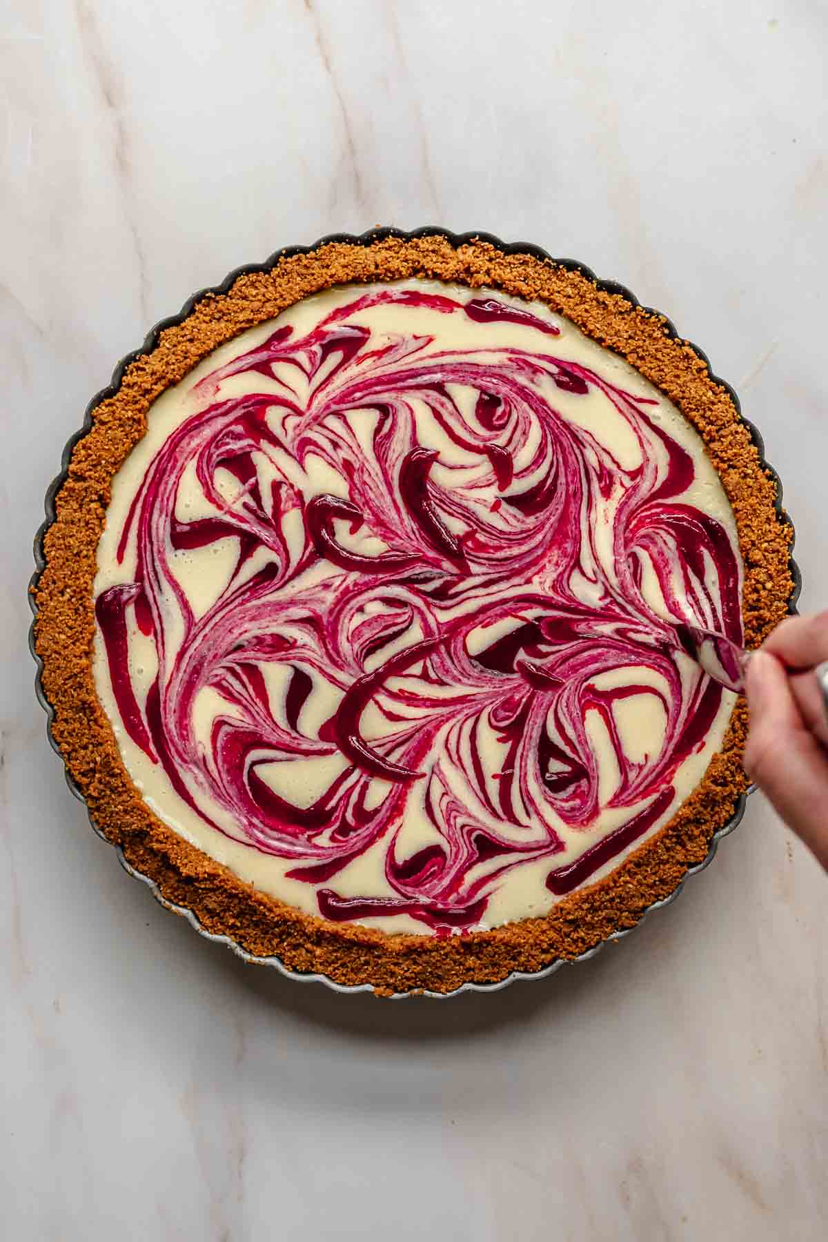 A knife swirls the cranberry puree through the white chocolate.