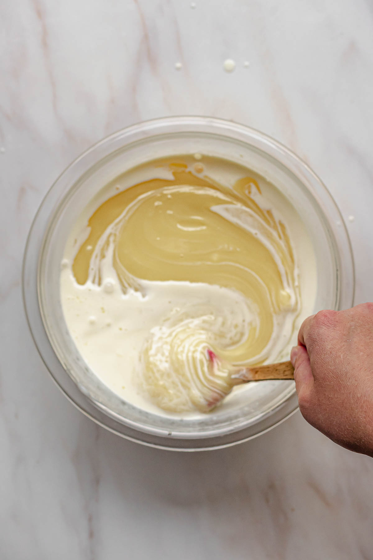 A hand mixes together melted white chocolate and heavy cream.