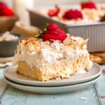 A slice of coconut tres leches cake on a plate with sliced strawberries on top.