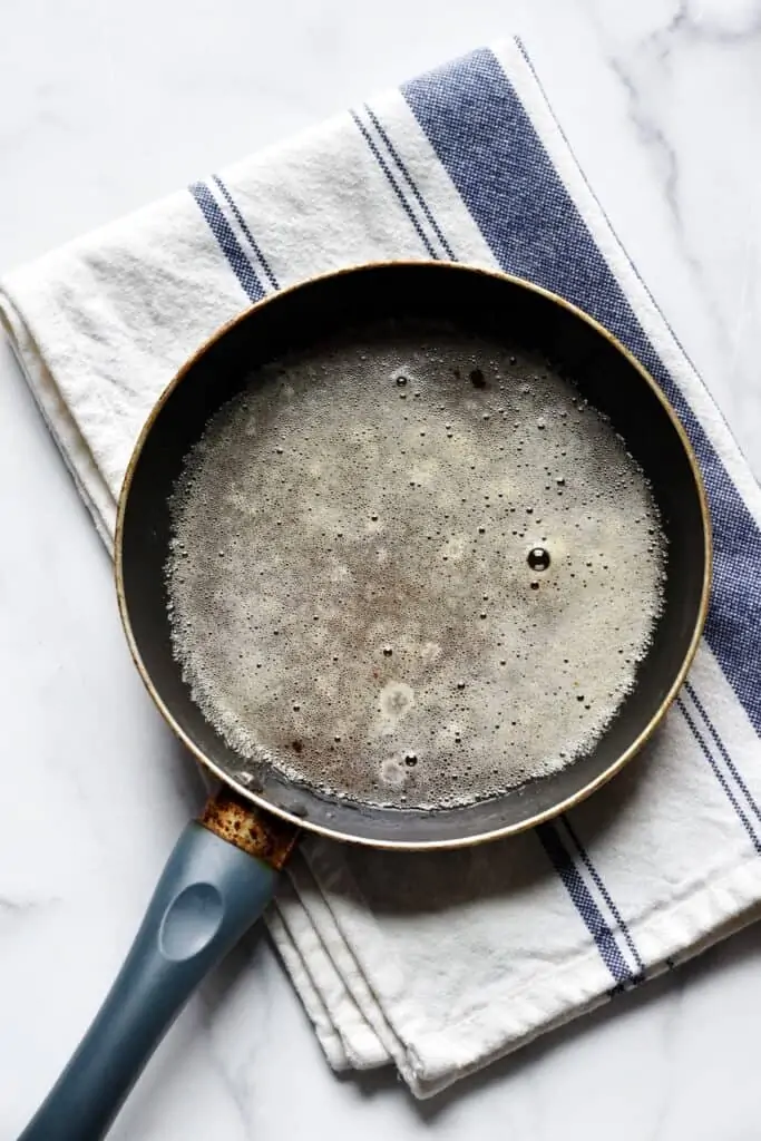 Over head shot of butter in a pan that has changed to a brown color and is only slightly foamy on top.