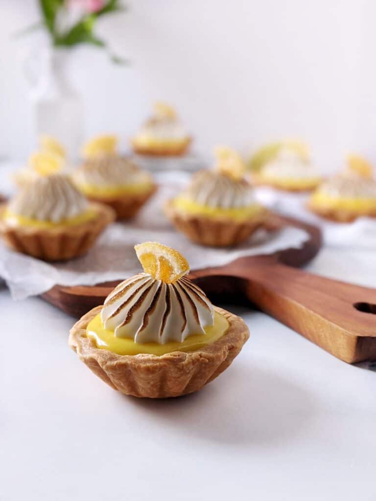 Straight on shot of one lemon meringue tartlet with multiple in the background.