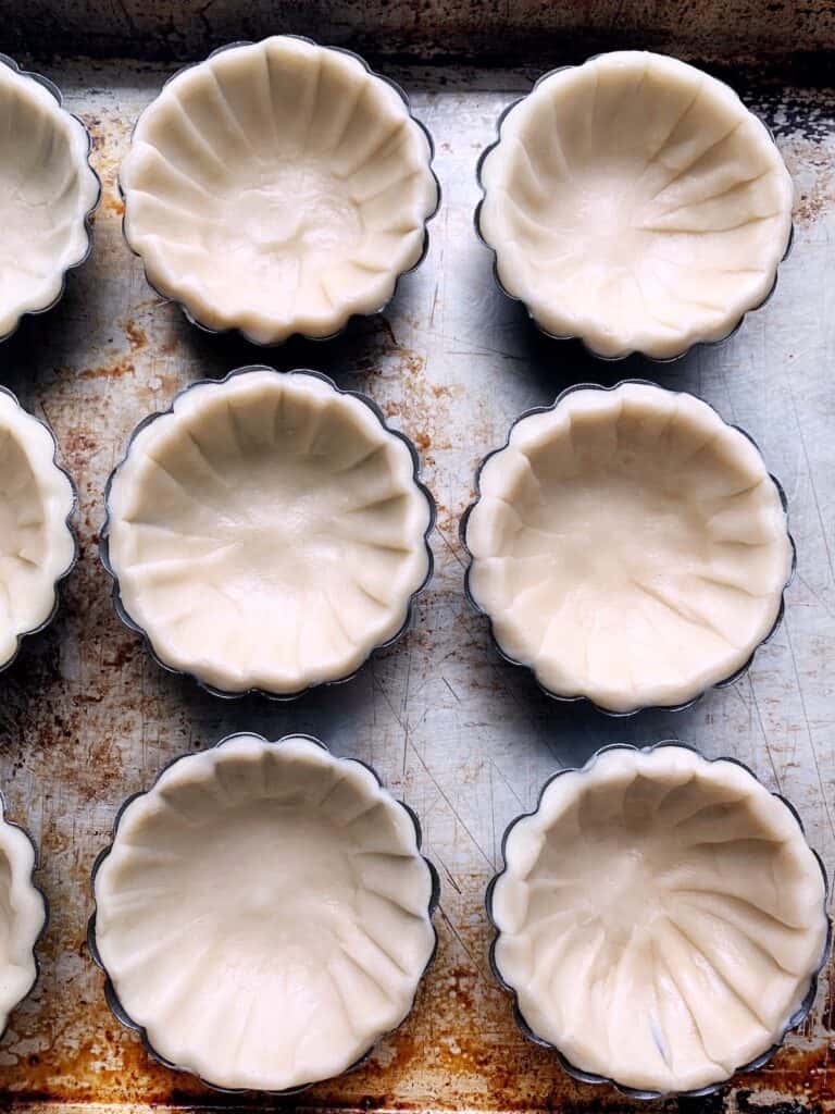 Overhead shot of raw dough in tartlets pans ready to be baked.