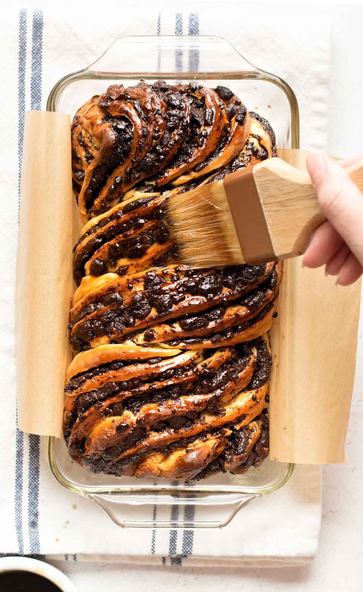 A pastry brush brushes espresso simple syrup on top of the babka loaf.